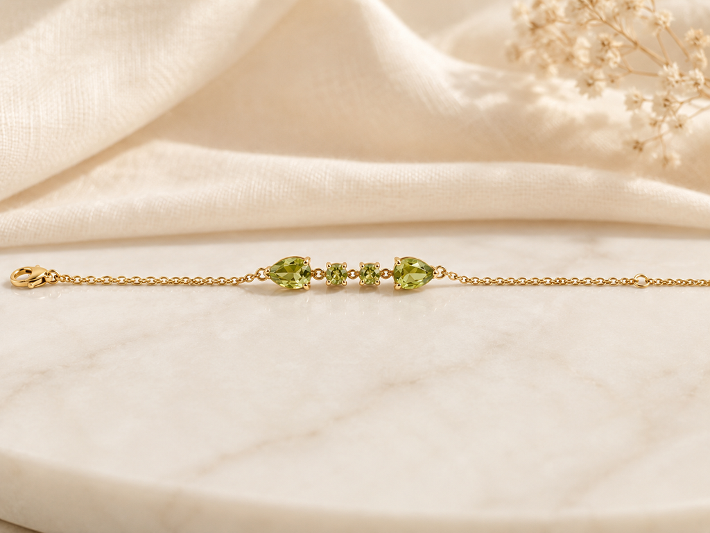 Solid 10k yellow gold bracelet chain with two pear-shaped and two round-shaped natural green peridot gemstones by Ophelisse, on a soft beige fabric background