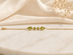 Solid 10k yellow gold bracelet chain with two pear-shaped and two round-shaped natural green peridot gemstones by Ophelisse, on a soft beige fabric background
