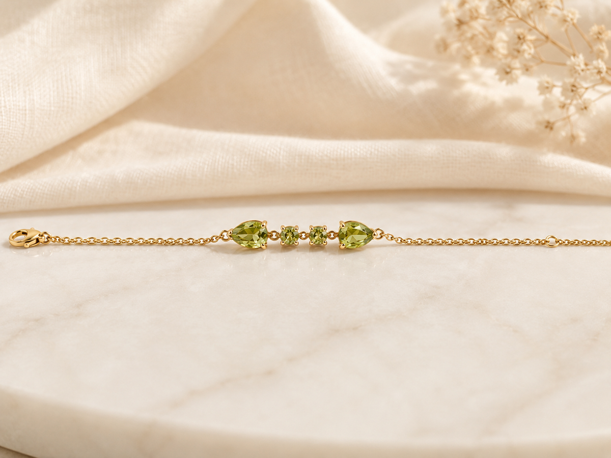 Solid 10k yellow gold bracelet chain with two pear-shaped and two round-shaped natural green peridot gemstones by Ophelisse, on a soft beige fabric background