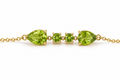 A close up view of Ophelisse solid 10k yellow gold bracelet featuring two pear-shaped and two round-shaped natural green peridot gemstones on a white background