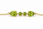 A close up view of Ophelisse solid 10k yellow gold bracelet featuring two pear-shaped and two round-shaped natural green peridot gemstones on a white background