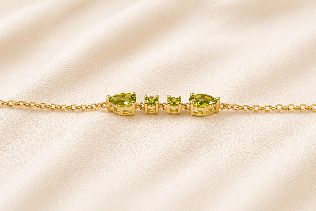 A close up view of Ophelisse gold chain bracelet with natural green peridot gemstones, side angle view, on a beige fabric background