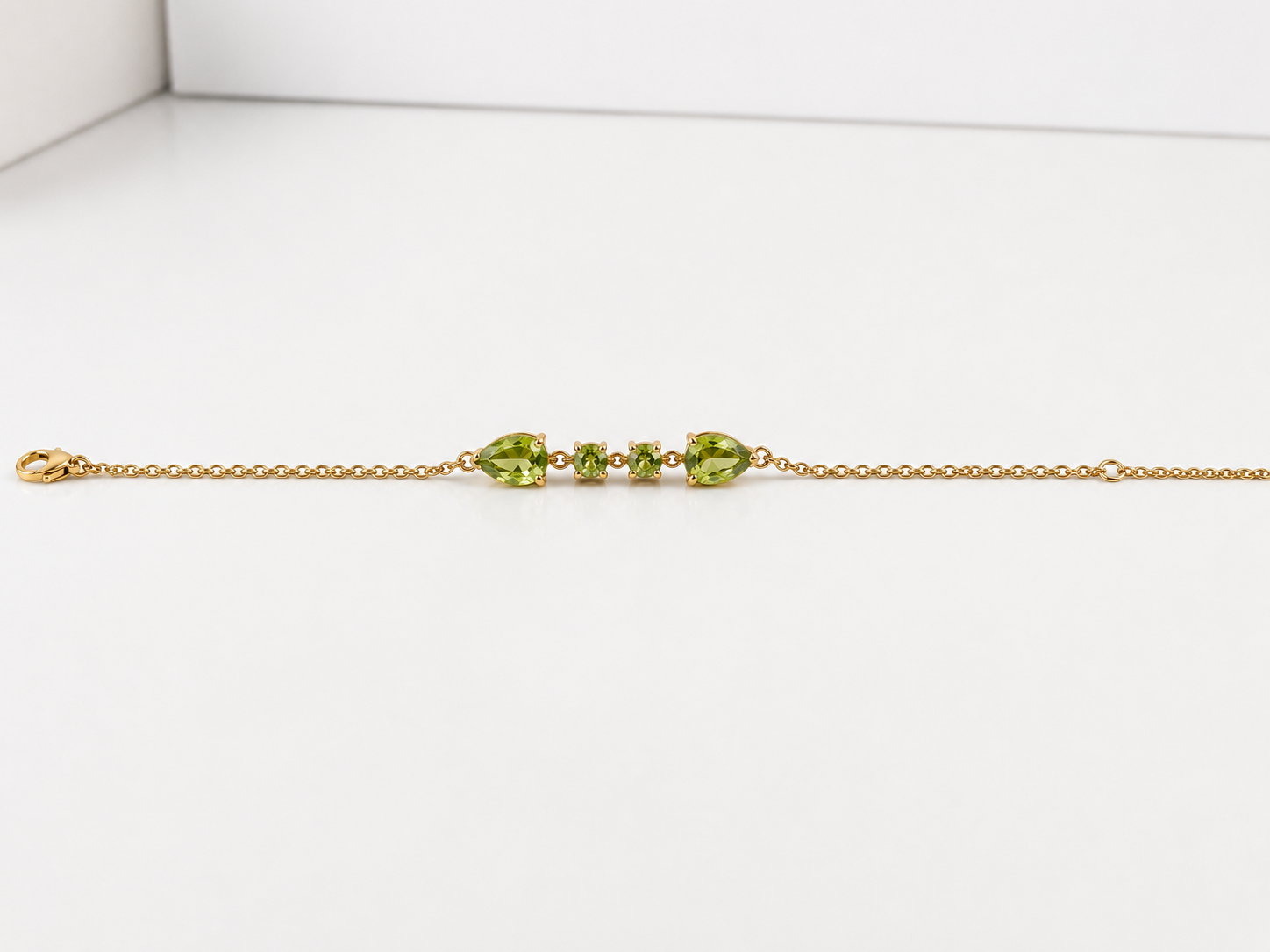 Ophelisse solid 10k yellow gold chain bracelet with natural green peridot gemstones, showing front view of two pear-shaped and two round-shaped stones, on a white background
