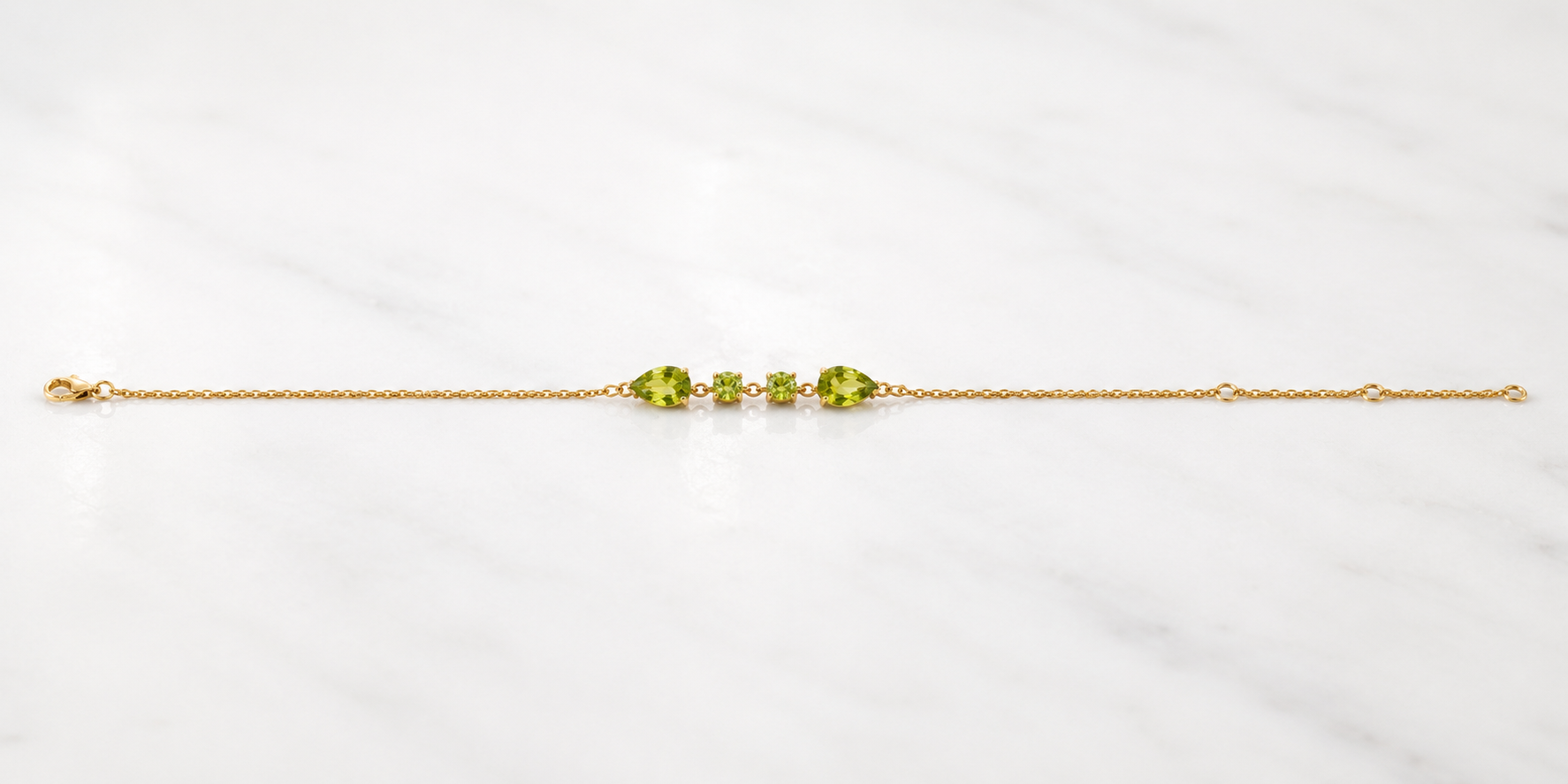 Full length view of Ophelisse solid 10k yellow gold chain bracelet with natural green peridot gemstones on a white marbled background