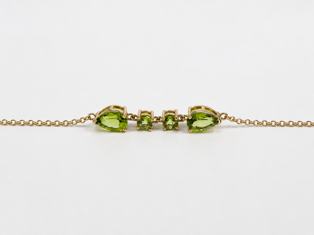A close up and side view of Ophelisse solid 10k yellow gold bracelet chain with two pear-shaped and two round-shaped natural green peridot gemstones, on a white background
