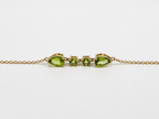 A close up and side view of Ophelisse solid 10k yellow gold bracelet chain with two pear-shaped and two round-shaped natural green peridot gemstones, on a white background