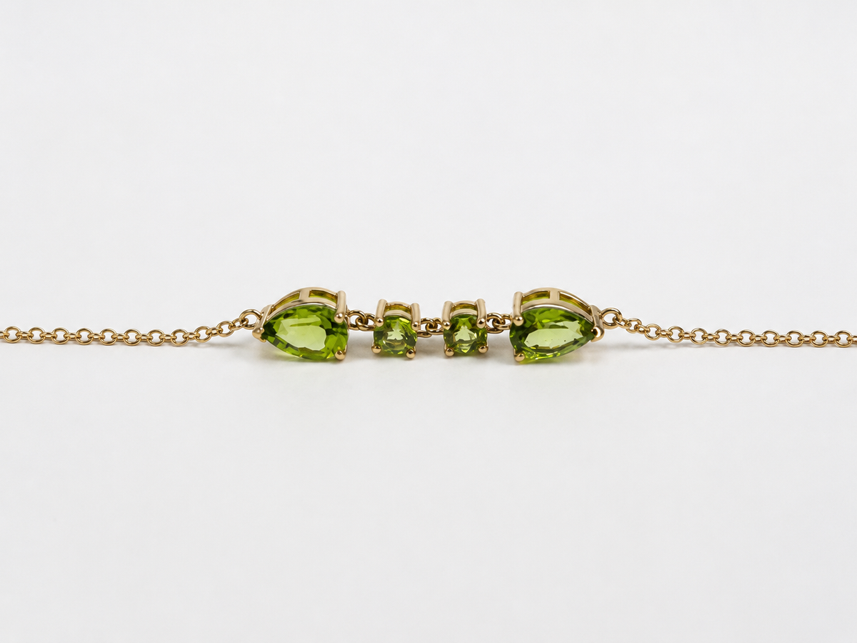 A close up and side view of Ophelisse solid 10k yellow gold bracelet chain with two pear-shaped and two round-shaped natural green peridot gemstones, on a white background