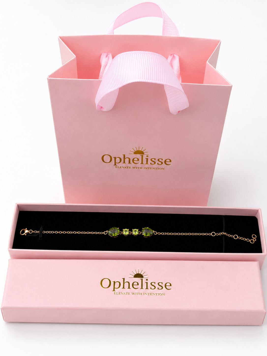 A solid 10k gold chain bracelet with natural green peridot gemstones presented in an open pink Ophelisse jewelry box, with a matching pink gift bag behind it on a white background.