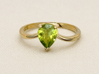 A solid 10k yellow gold ring featuring a pear-cut natural green peridot gemstone in a prong setting, displayed on a textured beige fabric background.