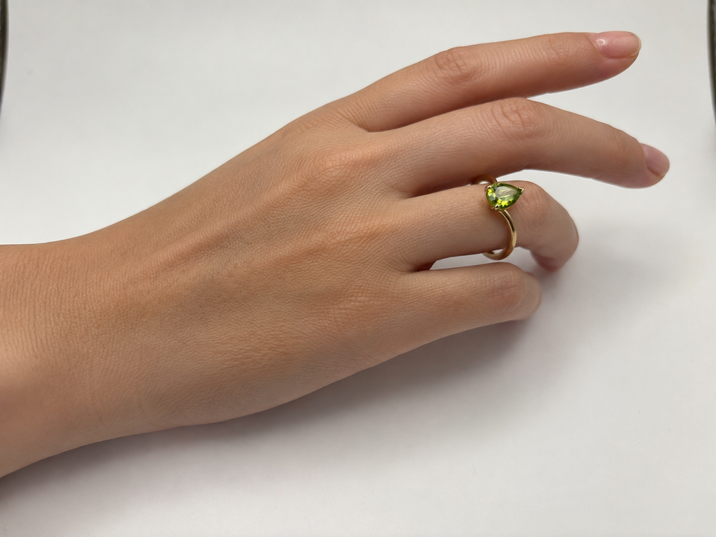 A solid 10k gold ring with a green heart-shaped natural peridot gemstone by Ophelisse worn on a person's ring finger, contrasted against a plain white background.