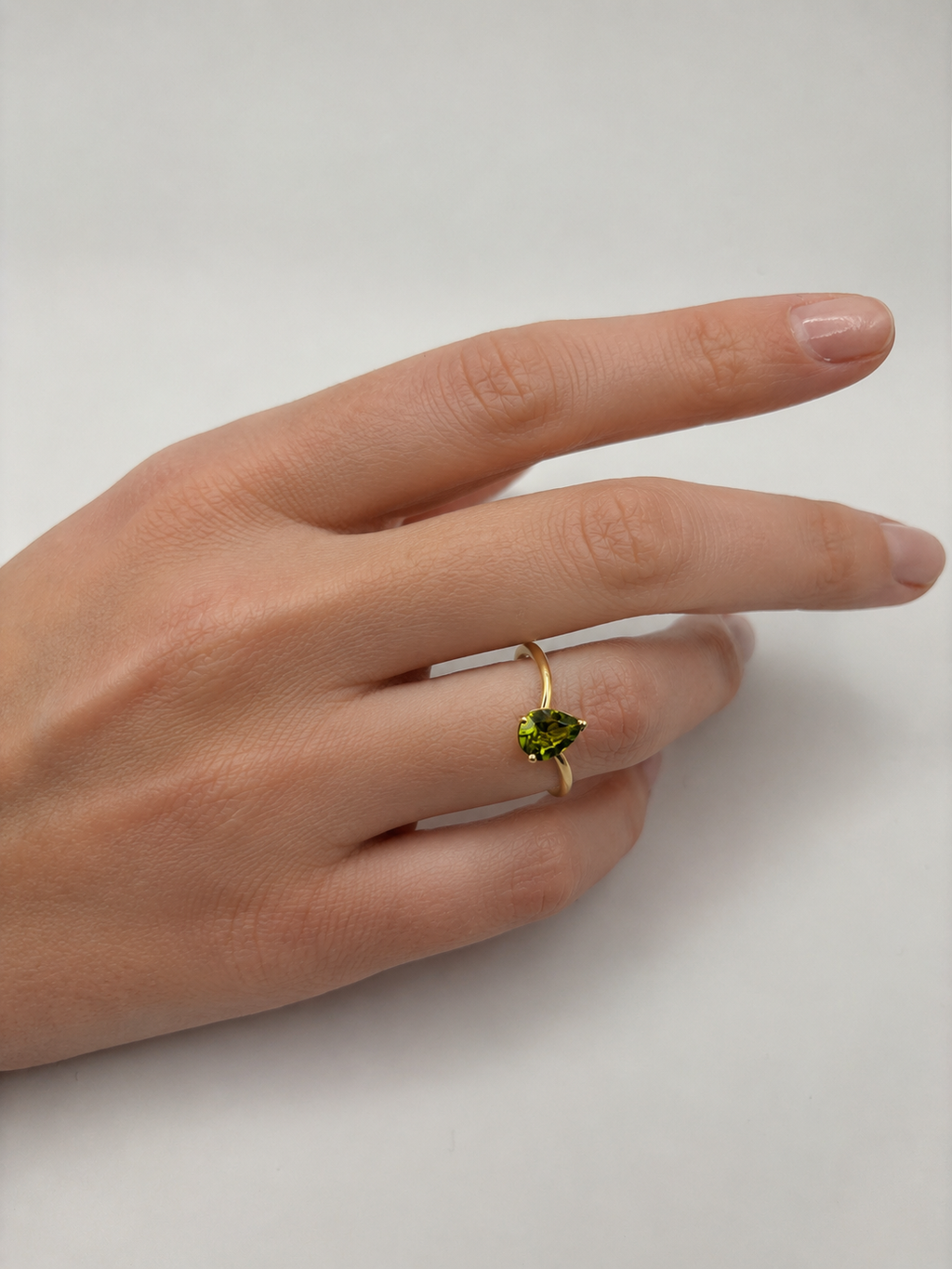 A 10k solid gold ring with a heart-shaped, natural green peridot gemstone by Ophelisse elegantly worn on a person's ring finger, shown against a plain light gray background.