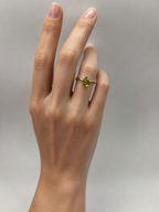 A close-up of a hand wearing a 10k solid  yellow gold ring with a pear-cut natural green peridot gemstone by Ophelisse, set against a soft gray background.