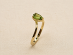 A 10k gold ring featuring a pear-cut green gemstone in a prong setting, displayed on an elegant textured sophisticated beige fabric background.