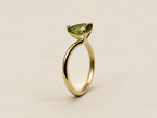A 10k yellow gold ring by Ophelisse featuring a marquise-cut green gemstone in a prong setting, displayed on an elegant textured off-white background.