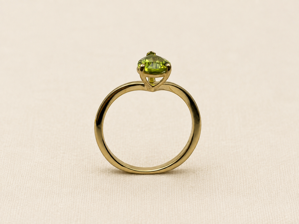 A 10k yellow gold ring with a single-cut light green gemstone by Ophelisse, displayed on an elegant textured beige fabric background.
