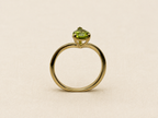 A 10k yellow gold ring with a single-cut light green gemstone by Ophelisse, displayed on an elegant textured beige fabric background.