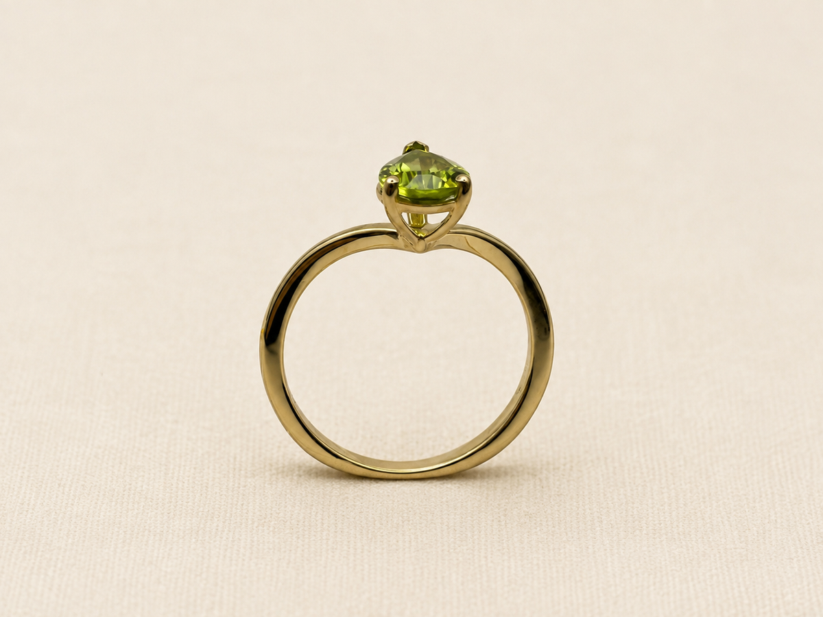 A 10k yellow gold ring with a single-cut light green gemstone by Ophelisse, displayed on an elegant textured beige fabric background.