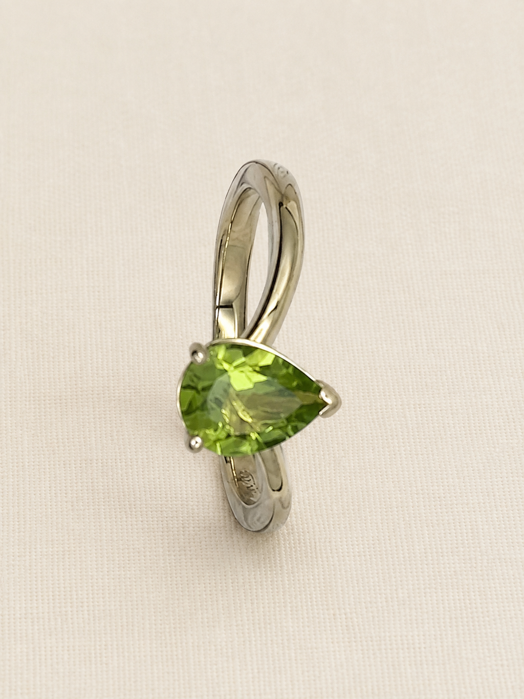 A solid 10k yellow ring featuring a pear-cut natural green peridot gemstone by Ophelisse, displayed on an elegant textured off-white background.