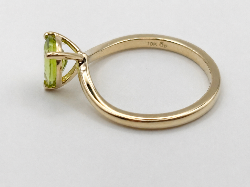 A solid yellow gold ring with a pear-cut natural peridot gemstone by Ophelisse, shown from a side profile on a light gray background. The inner band is stamped with '10K OP'.