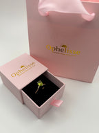 A solid 10k yellow gold ring with a natural green peridot gemstone displayed in an open pink Ophelisse jewelry box, with a matching pink Ophelisse shopping bag for a luxury shopping experience.
